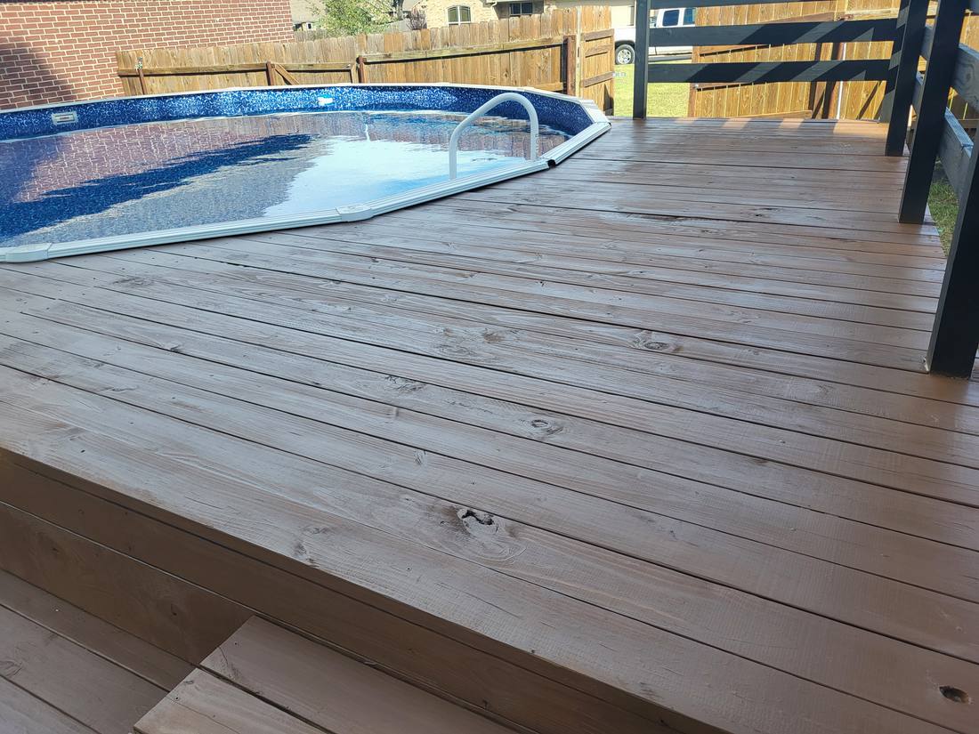 Finished above-ground pool deck with dark stained decking and black horizontal-slat privacy rail