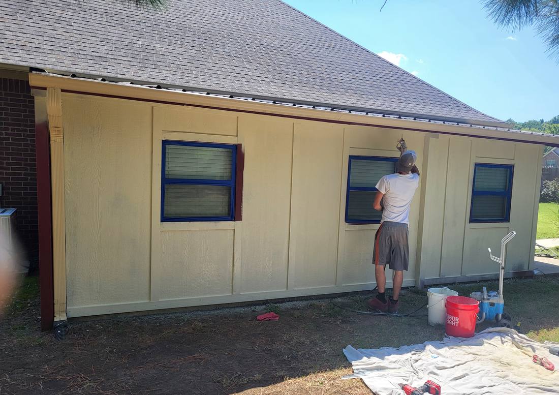 Crew member spray-painting the exterior trim of a house